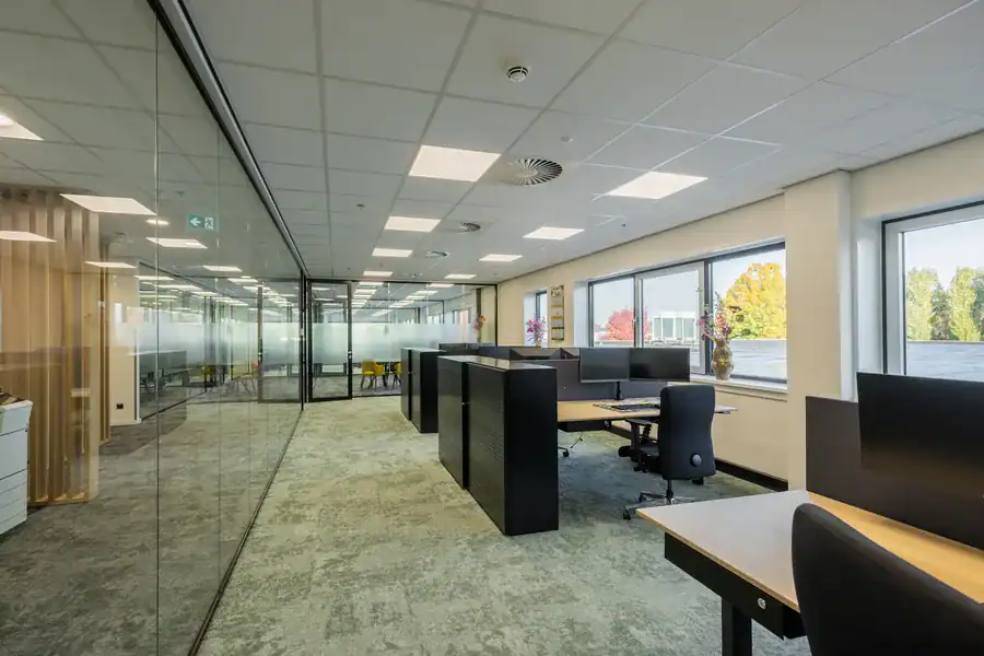 Open kantoorruimte met werkplekken op een tapijttegelvloer in een bedrijfspand